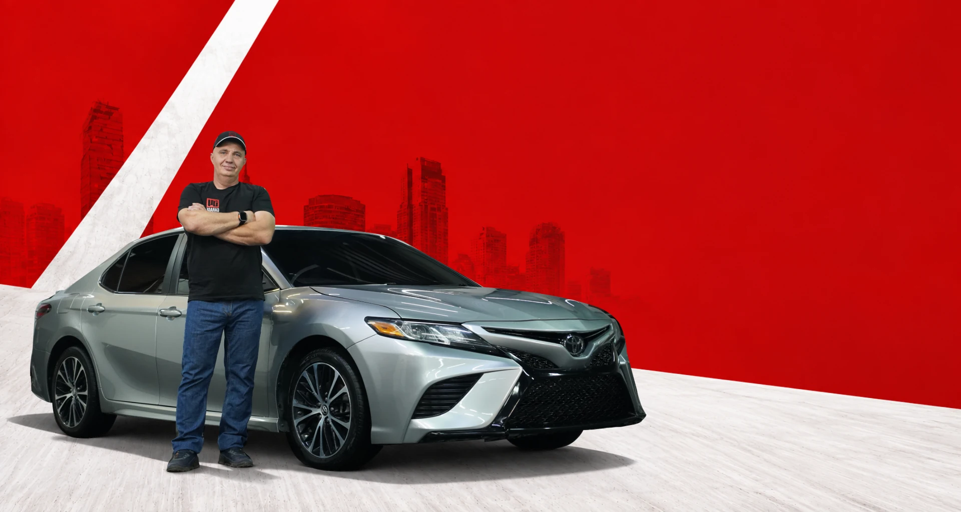 Влад рядом с серебристой Toyota Camry 2018 на красном городском фоне